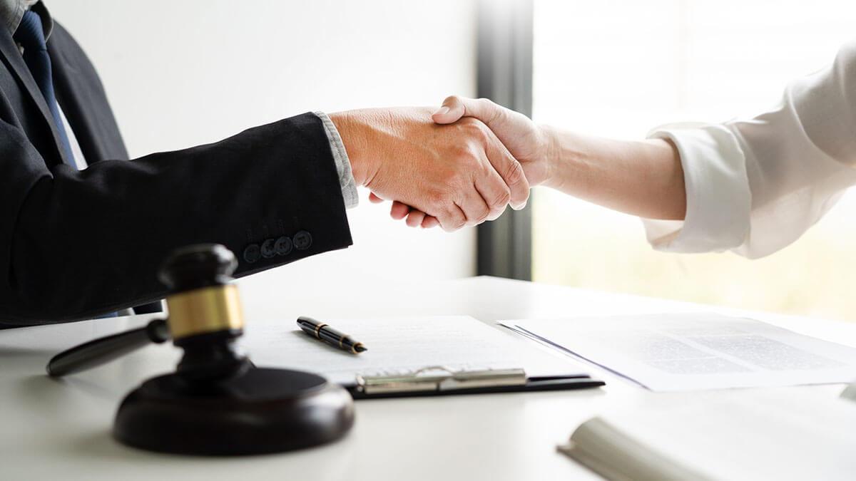 Two people shaking hands with a gavel in frame in the foreground