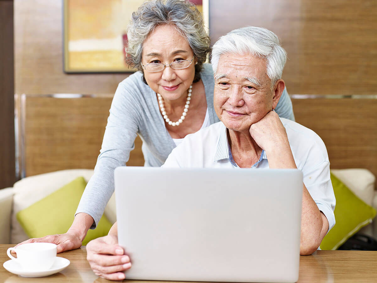 An elderly asaian couple looking at a laptop screen and smiling