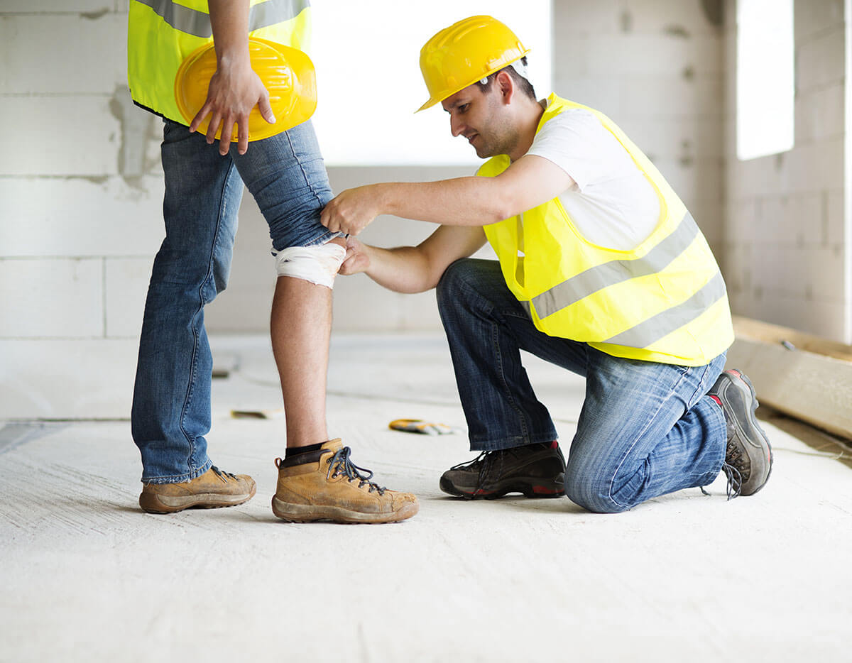 A construction worker kneeled down to wrap a bandage around another construction workers leg